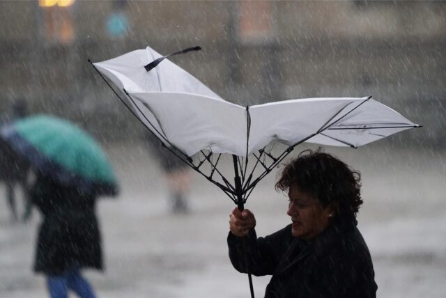 Mit einem Regenschirm versucht sich eine Frau bei stürmischem Wetter gegen den Regen zu schützen.