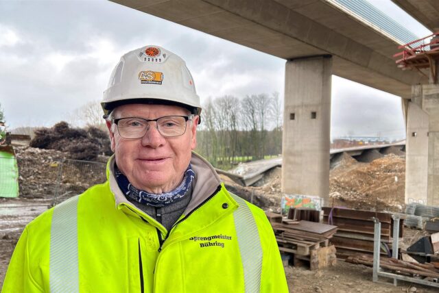 Karl-Heinz Bühring, der 73-Jährige Sprengmeister, steht vor dem äußeren Teilbauwerk der Liedbachtalbrücke in der Massener Heide in Unna. Der Sprengmeister trägt eine gelbe Warnweste und einen weißes Schutzhelm.