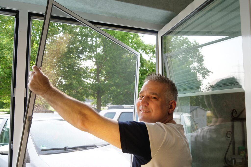 Mann setzt Fliegengitter in Fenster ein