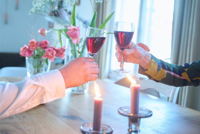 Ein Paar stößt an einem für Valentinstag dekorierten Tisch mit Rotwein an.