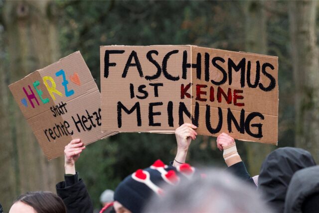 Menschen halten bei einer Kundgebung Schilder hoch.