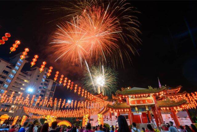 Zu einer Feier des Chinesischen Neujahrsfests sind am Abend viele Menschen unterwegs. Es findet ein Feuerwerk statt, die Straßen sind mit roten Laternen geschmückt und im Hintergrund wird ein Drachentanz veranstaltet.