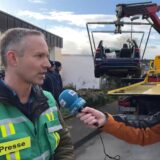 Kevin Kohues (l.), Pressesprecher der Stadt Unna, spricht mit Reporter Thomas Raulf. Im Hintergrund wird ein Autowrack auf einen Abschleppwagen geladen.