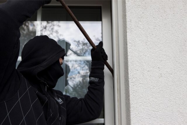 Ein als Einbrecher verkleideter Mann hebelt mit einem Brecheisen ein Fenster auf.