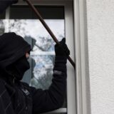 Ein als Einbrecher verkleideter Mann hebelt mit einem Brecheisen ein Fenster auf.