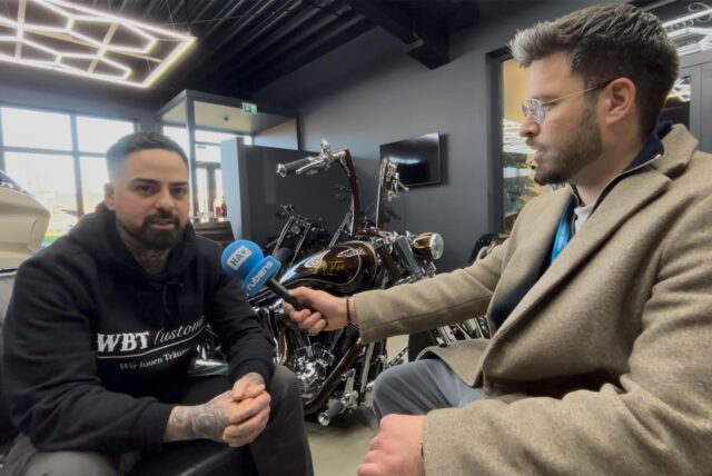 Siya Shokohi, Inhaber von WBT Customs in Holzwickede im Interview mit HA-Reporter Stefan Schier. Shokohi ist an den Händen und am Hals tätowiert. Er trägt einen schwarzen Pullover. Der HA-Reporter trägt einen hellen Mantel und eine Brille.