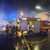 Ein Feuerwehrfahrzeug steht bei einem nächtlichen Einsatz auf einem Firmengelände.