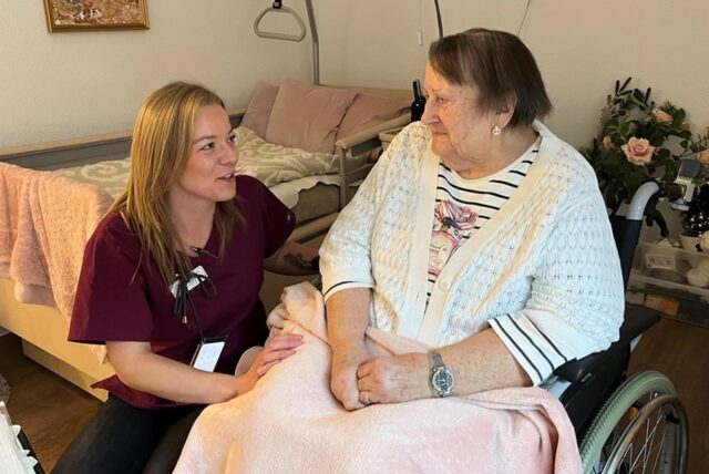 Pflegerin hockt neben Bewohnerin