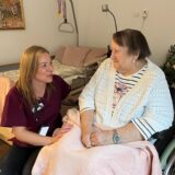 Pflegerin hockt neben Bewohnerin
