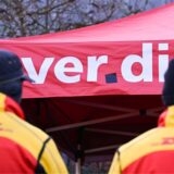 Zwei Mitarbeiter des Logistikkonzerns DHL stehen an einem Warnstreik-Posten der Gewerkschaft Verdi, der sich am Eingang einer DHL-Zustellbasis befindet.