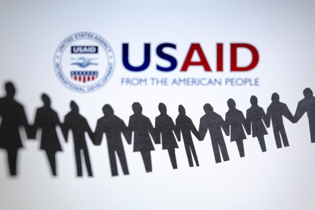 Das Logo der US-Entwicklungsbehörde, United States Agency for International Development (USAID), ist hinter einer Kette von ausgeschnittenen Papierfiguren zu sehen.
