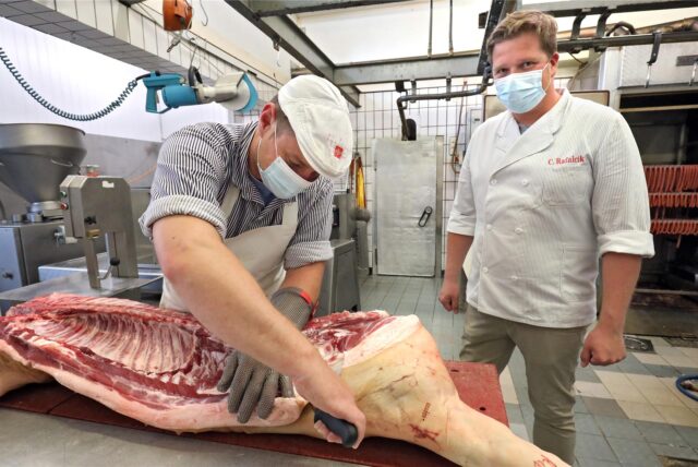 Metzgermeister Christian Rafalcik (r.) sieht einem Mitarbeiter beim Zerlegen einer Schweinhälfte in seinem Betrieb in Fröndenberg zu.