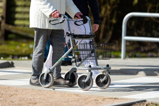 Ein Senior, der mit einem Rollator auf einem gehweg unterwegs ist.