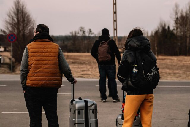 Geflüchtete Menschen stehen mit Koffern am Straßenrand (Symbolbild).