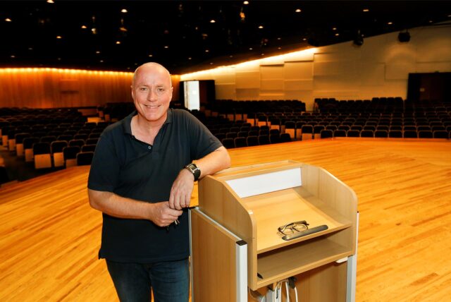 Kamens Kulturplaner Jörg Höning steht in der Konzertaula in Kamen, einen Arm auf ein Rednerpult abgestützt.
