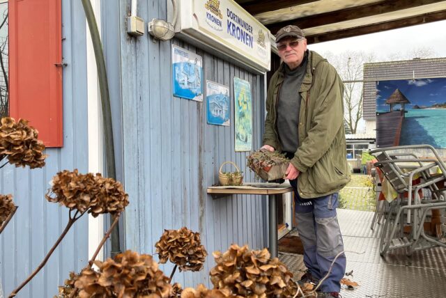 Jörg Scholz steht in seinem Garten in Königsborn vor einem hellblau angestrichenen Bauwagen, der zur Gartenhütte umfunktioniert worden ist.