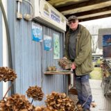 Jörg Scholz steht in seinem Garten in Königsborn vor einem hellblau angestrichenen Bauwagen, der zur Gartenhütte umfunktioniert worden ist.