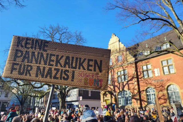 Ein Pappschild mit der Aufschrift „Keine Pannekauken für Nazis!“ wird bei einer Demo gegen Rechts in Schwerte hochgehalten. Viele Menschen haben sich dafür auf dem Postplatz versammelt.