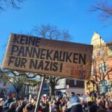 Ein Pappschild mit der Aufschrift „Keine Pannekauken für Nazis!“ wird bei einer Demo gegen Rechts in Schwerte hochgehalten. Viele Menschen haben sich dafür auf dem Postplatz versammelt.