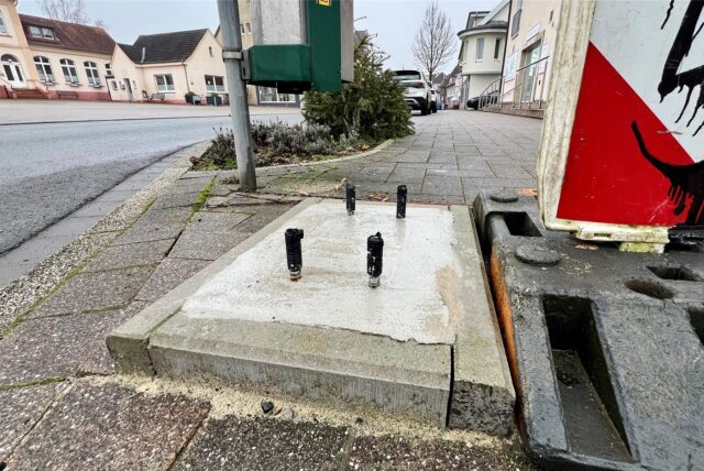 Aus einem Betonfundament in einem Gehweg in Unna ragen drei schwarze Metallstangen. Daneben steht eine Bake