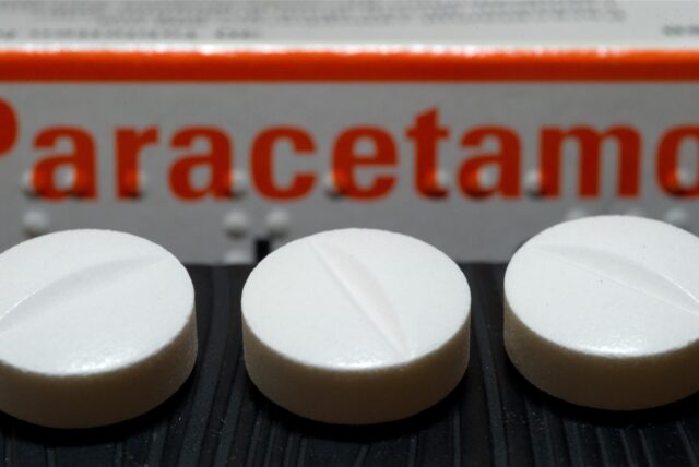 Vor einer Arzneiverpackung liegen Tabletten, die den Wirkstoff Paracetamol enthalten.