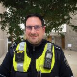 Polizeihauptkommissar Dennis Kischel ist der neue Bezirksdienstbeamte in Holzwickede. Hier steht er im Atrium des Holzwickeder Rat- und Bürgerhauses. Er trägt eine Polizei Uniform und eine Brille.