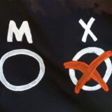 Auf schwarzem Hintergrund stehen in weißer Schrift die Kürzel W, M und X – der Kreis unter dem X ist angekreuzt mit einem roten X.