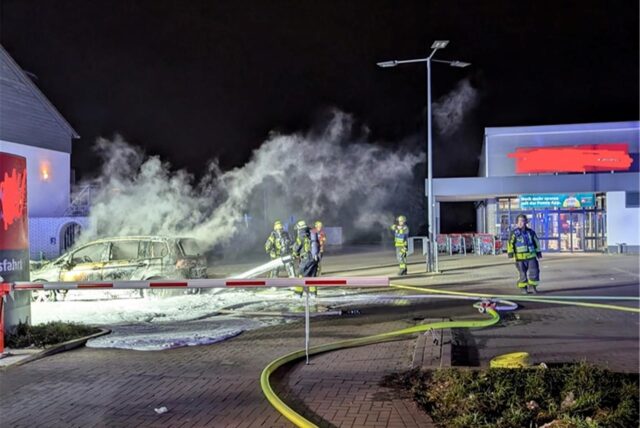 Feuerwehrleute löschen auf dem Parkplatz von Penny in Bergkamen ein brennendes Auto mit Schaum.