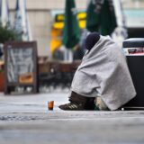 Ein Bettler sitzt mit einer Decke bedeckt am Straßenrand.
