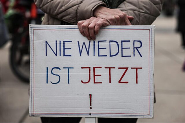 Ein Demonstrant hält ein Plakat mit der Aufschrift „Nie wieder ist jetzt“ (Archivbild).