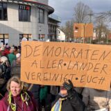 Bei einer Kundgebung auf dem Rathausvorplatz in Unna hält eine Demonstrantin ein Schild hoch mit der Aufschrift: Demokraten aller Länder, vereinigt Euch!
