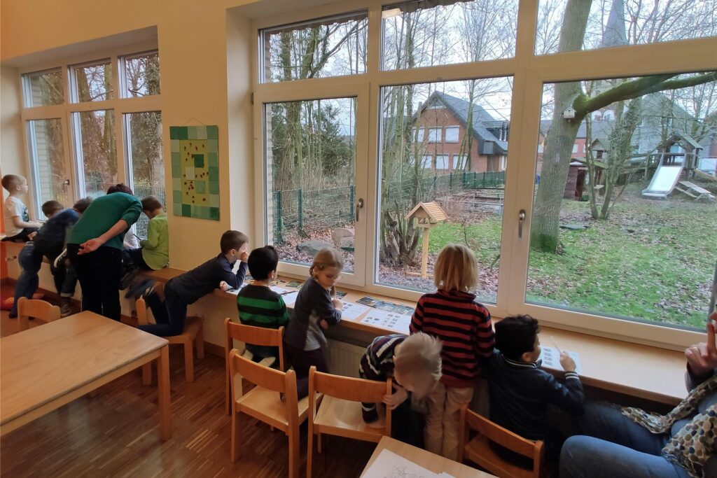 Kinder sitzen in einer Tageseinrichtung am Fenster und blicken nach draußen. Kinder sitzen in einer Tageseinrichtung am Fenster und blicken nach draußen.