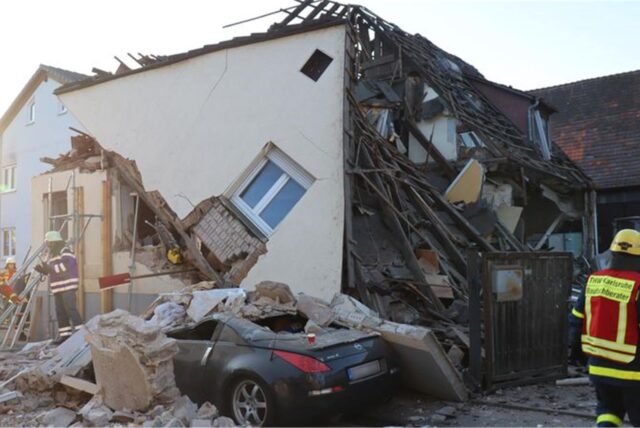 Vor einem eingestürzten Haus steht ein Cabrio. Einsatzkräfte sind vor Ort.