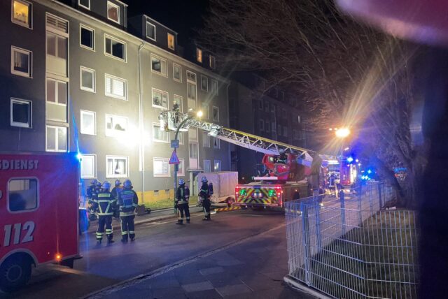 Feuerwehrleute und Feuerwehrautos stehen während eines Brandeinsatzes vor einem Haus in der Dortmunder Nordstadt.