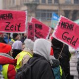 Menschen protestieren mit roten Schildern, mit denen sie mehr Geld fordern.
