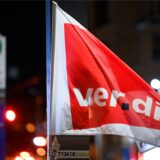 Eine Fahne der Gewerkschaft Verdi weht vor einer Bushaltestelle.