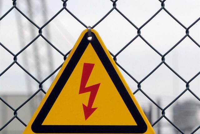 Ein Blitz-Symbol für Elektrizität hängt an einem Maschendrahtzaun.