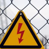Ein Blitz-Symbol für Elektrizität hängt an einem Maschendrahtzaun.