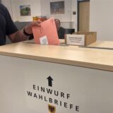 Ein Wahlbrief wird in eine Wahlurne eingeworfen.