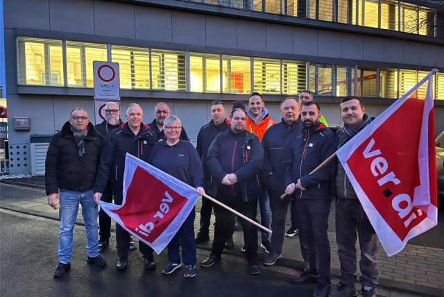 Männer und Frauen, die bei der VKU am Standort Kamen arbeiten, stehen streikend vor dem Firmengebäude an der Lünener Straße in Kamen.