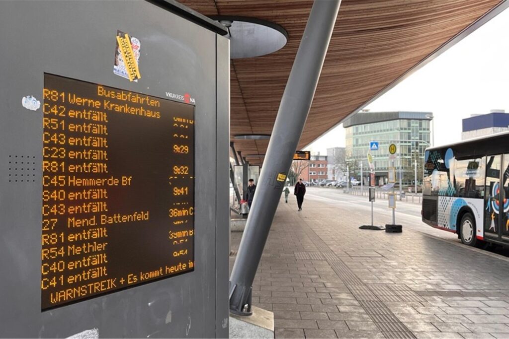 Auf einer Anzeige am Busbahnhof in Unna steht, welche Busabfahrten alle entfallen. Ein Bus steht an der Haltestelle.