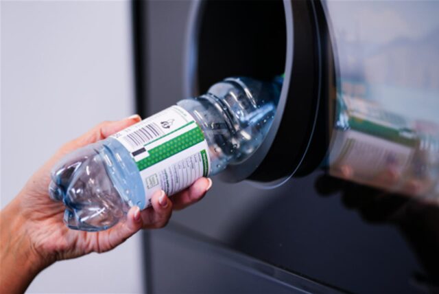 Eine Hand legt eine Pfandflasche in einen Automaten