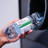 Eine Hand legt eine Pfandflasche in einen Automaten