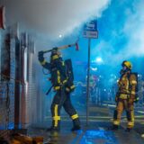 Ein Feuerwehrmann schlägt mit einer Axt die Tür einer Gaststätte in Menden auf, aus der Rauch kommt.