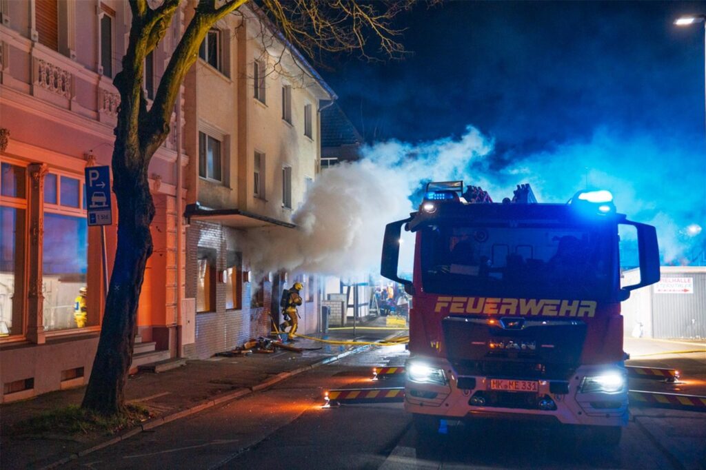 Ein Feuerwehrauto und EInsatzkräfte an einer Gaststätte in Menden, aus deren Fenster Rauch kommt.