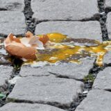 Nahaufnahme von einem zerbrochenen Ei auf Kopfsteinpflaster.