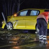 Ein gelbes Auto ist nach einem Unfall beschädigt, ein Mann mit einer Warnweste fegt Trümmer zusammen.