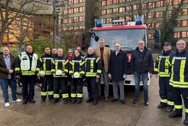 Feuerwehrleute sowie Mitarbeiter von Stadtverwaltung und Steag stehen auf dem Platz der Partnerstädte vor einem Feuerwehrfahrzeug, das vor dem Rathaus parkt.