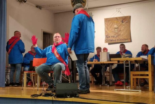 „Sup-Peiter“ bei der Nachbarschaft Westeneicken 2025: Die Männer in den blauen Oberteilen mit den roten Halstüchern verhandeln auf der Bühne des evangelischen Gemeindehauses in Schwerte-Westhofen.