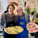 Zwei Personen präsentieren jeweils eine Platte mit Speisen. Eine Person hält eine Platte mit Wurstwaren und die andere eine Platte mit Käse.
